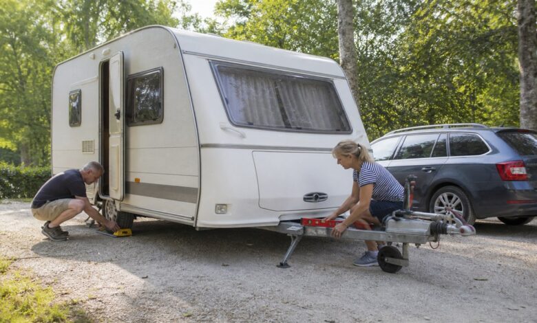 Paar richtet einen Wohnwagen mit Wasserwaage und Unterlegkeilen aus