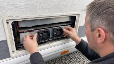 Techniker montiert zwei Lüfter hinter dem Kühlschrankgitter eines Wohnwagens