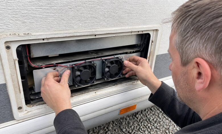 Techniker montiert zwei Lüfter hinter dem Kühlschrankgitter eines Wohnwagens
