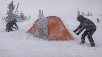 Zwei Wintercamper sichern ein Expeditionszelt im Schneesturm