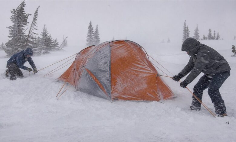 Zwei Wintercamper sichern ein Expeditionszelt im Schneesturm
