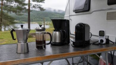 Vier unterschiedliche Kaffeezubereiter auf einem Campingtisch vor einem Wohnwagen