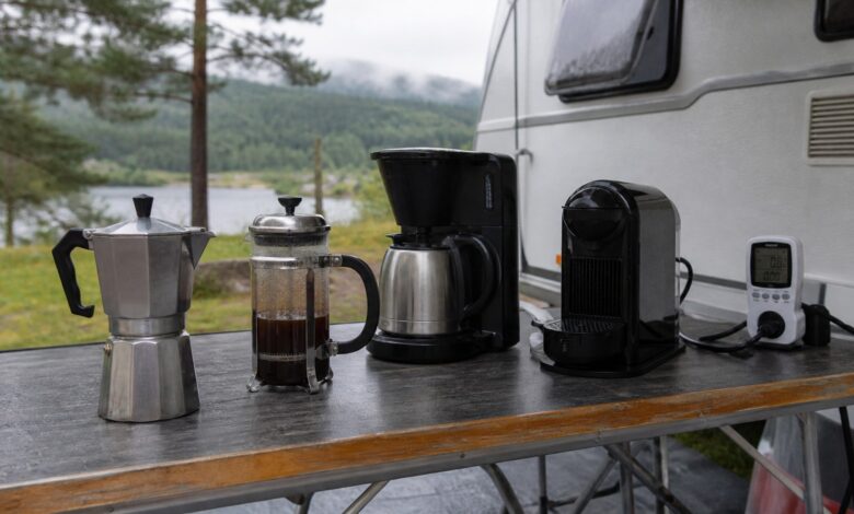 Vier unterschiedliche Kaffeezubereiter auf einem Campingtisch vor einem Wohnwagen
