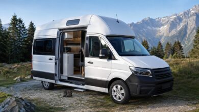 Weißer Hochdach-Campervan mit geöffneter Schiebetür auf einem Alpenstellplatz