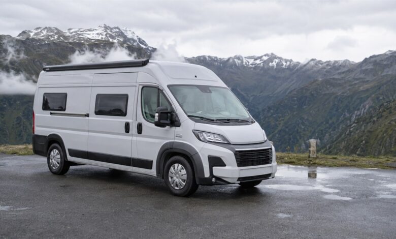 Weißer Hochdach-Campervan auf einem nassen Alpenparkplatz