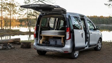 Silberner Kompaktvan mit geöffnetem Heck und einfachem Minicamper-Ausbau am See