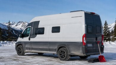 Weiß-grauer Hochdach-Campervan mit Winterreifen auf einem verschneiten Bergparkplatz