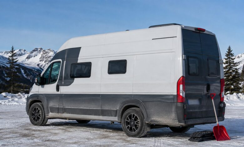 Weiß-grauer Hochdach-Campervan mit Winterreifen auf einem verschneiten Bergparkplatz