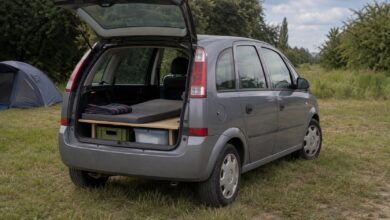 Älterer grauer Kompaktvan mit geöffneter Heckklappe und einfacher Schlafplattform
