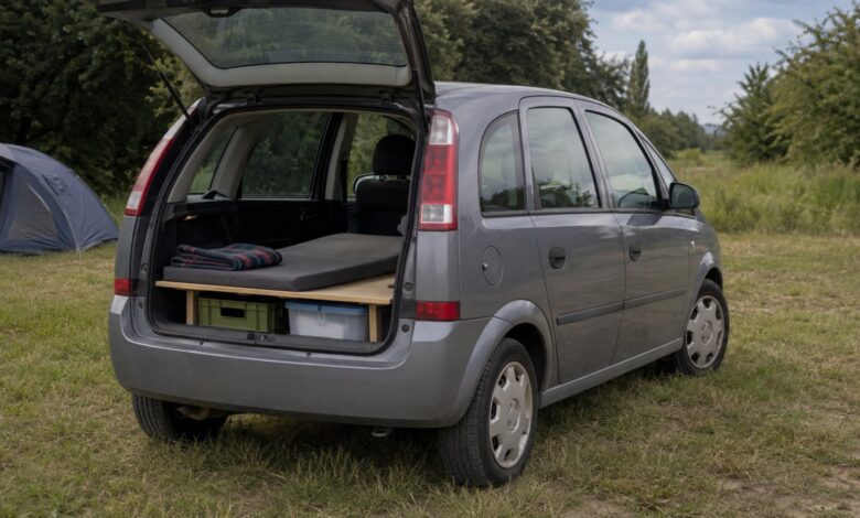 Älterer grauer Kompaktvan mit geöffneter Heckklappe und einfacher Schlafplattform