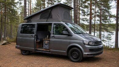 Grauer Campingvan mit gerade geöffnetem Aufstelldach und offener Schiebetür am See