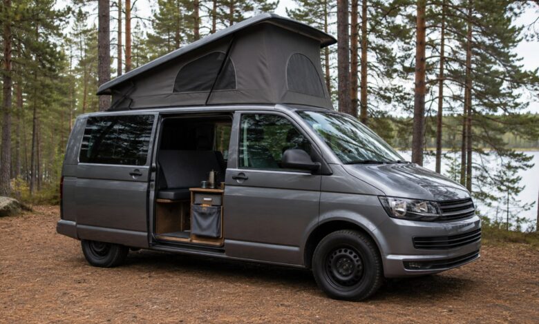 Grauer Campingvan mit gerade geöffnetem Aufstelldach und offener Schiebetür am See