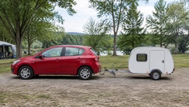 Kleiner weißer Einachs-Wohnwagen mit gerader A-Deichsel hinter einem roten Kompaktwagen