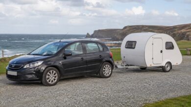 Kleiner weißer Einachs-Wohnwagen mit gerader A-Deichsel hinter einem dunklen Kompaktwagen